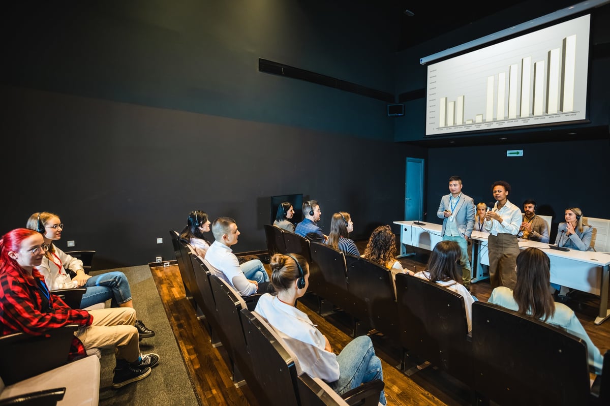 Asian and African American business people having speach on a press conference in a convention center. Diagrams on a smartboard