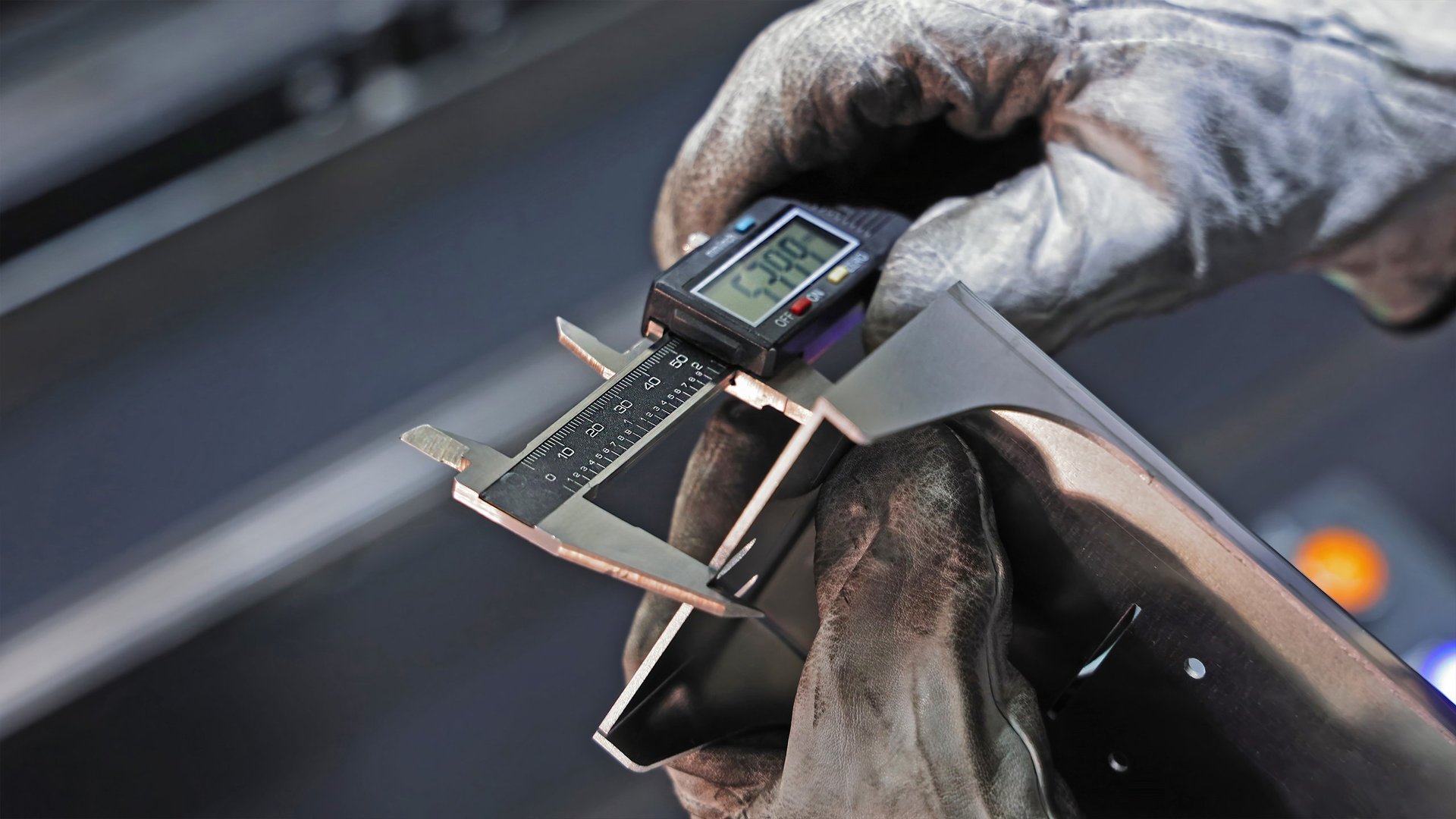Worker measuring metal part with digital caliper showing precise measurement of 53.09 millimeters