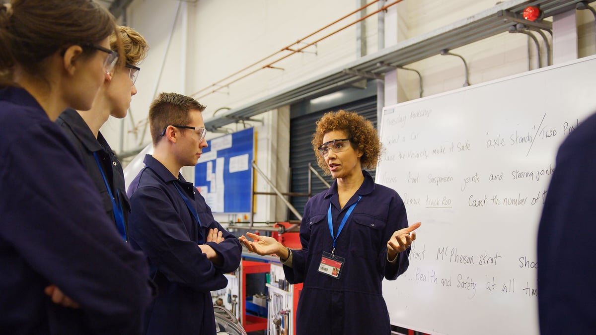 Female Tutor By Whiteboard With Students Teaching Auto Mechanic Apprenticeship At College