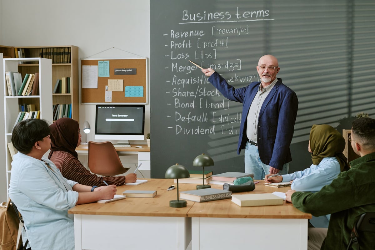 Senior Caucasian male teacher explaining business terms to migrant students, supporting language learning and economic integration