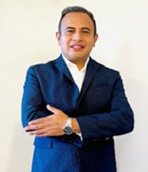 Professional man in dark blue blazer and white dress shirt with arms crossed, smiling at camera against neutral background
